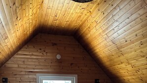 Et soveværelse med skråvæg, et vindue, en seng, et natbord, en lampe og en kommode.