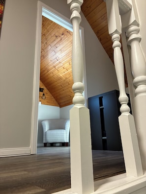 A staircase with white balusters leading to a room with a wooden ceiling and a patterned chair.