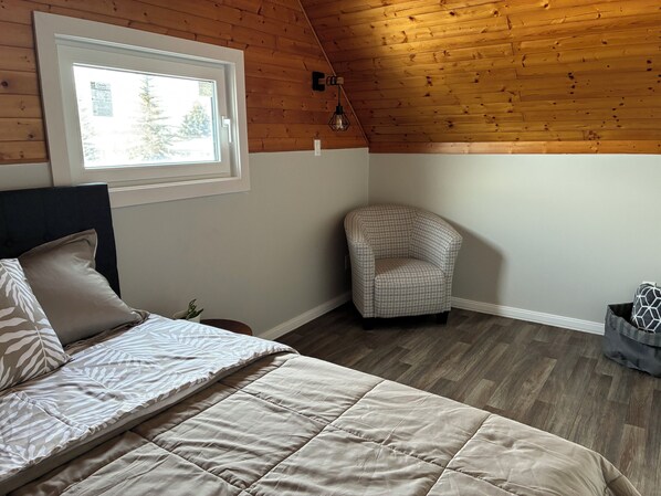 A bedroom with a bed, a chair, a window, and wooden ceiling.
