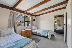 A bedroom with two beds, a wooden dresser, and a window with curtains. - Ward Cottage - Wanaka Holiday Home (Wanaka)