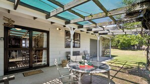 Eine überdachte Terrasse mit Glasdach, Sitzgelegenheiten im Freien und Blick auf den Garten.
