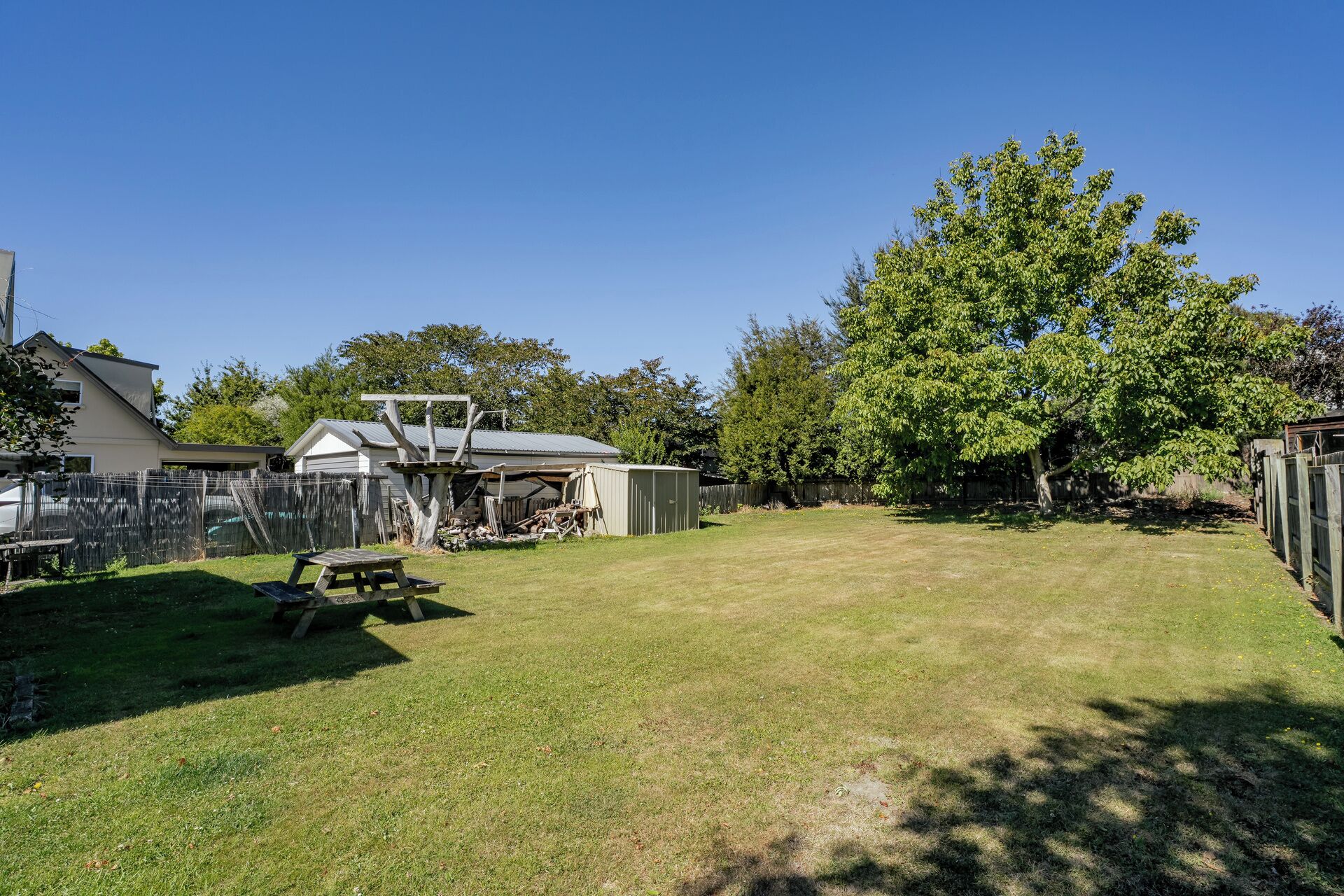 A backyard with a picnic table, a shed, and a large tree.