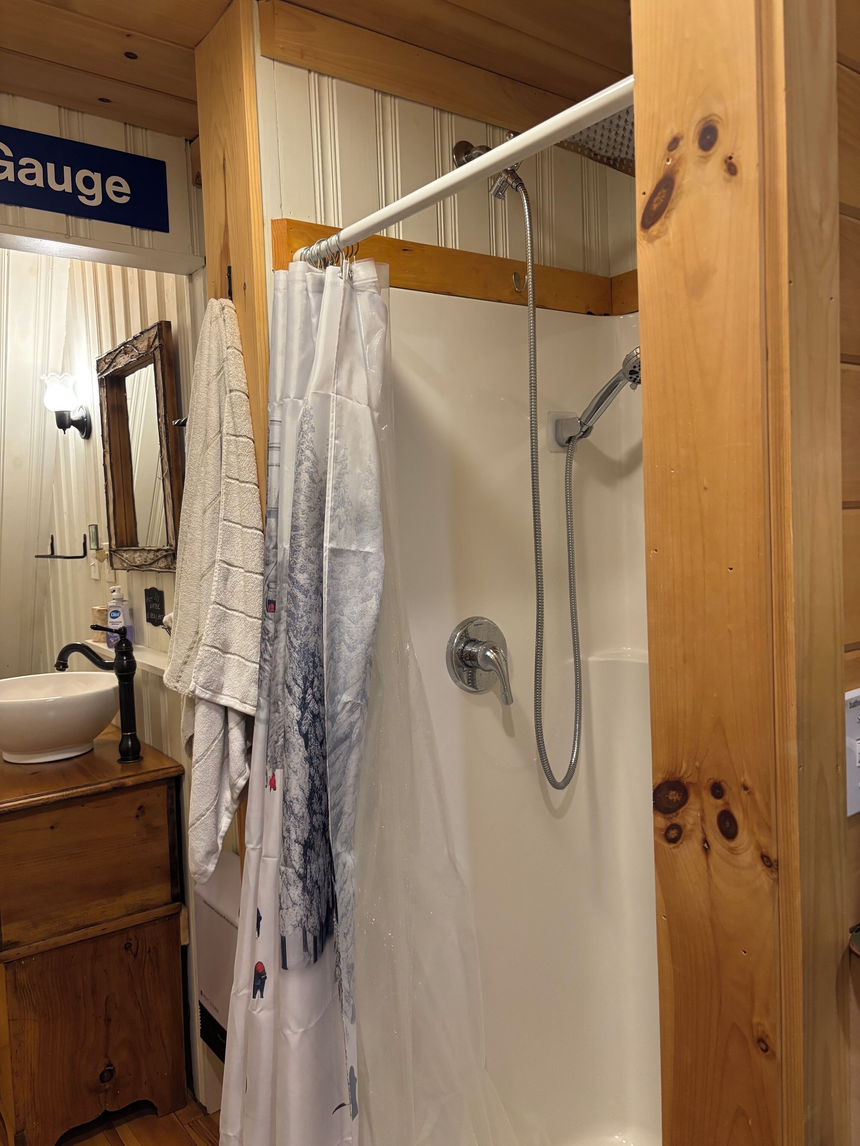 A bathroom with a wooden vanity, a sink, a mirror, a shower with a handheld showerhead, and a towel hanging on the wall.