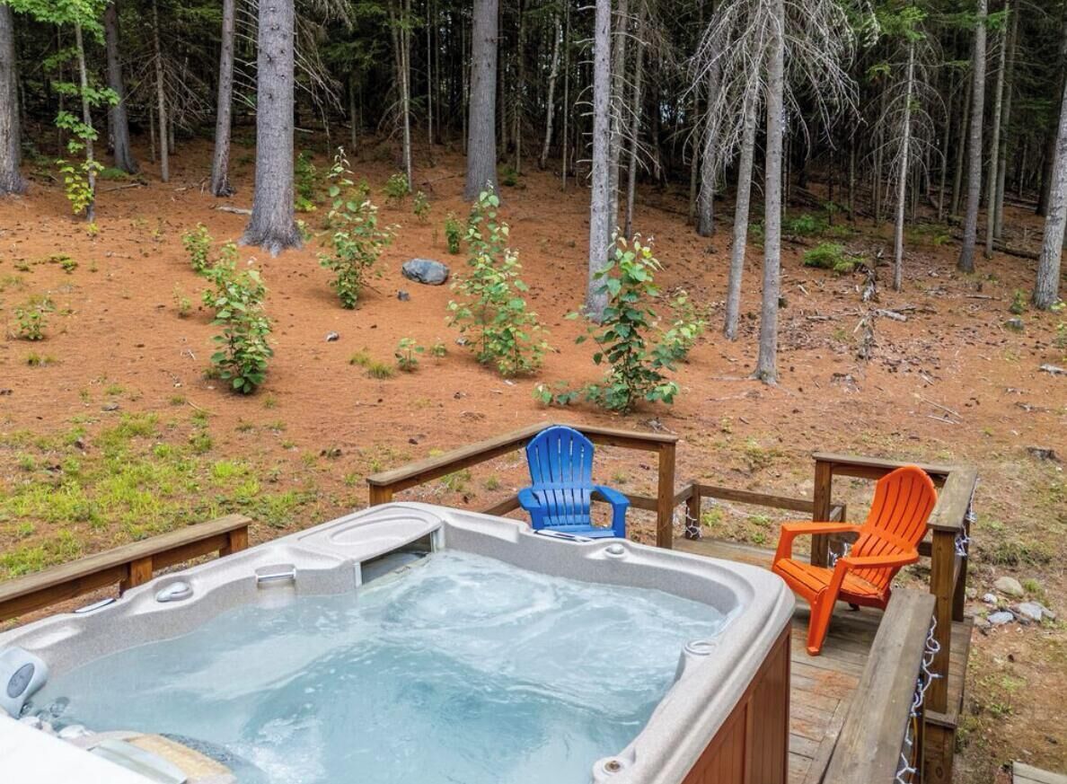 Ein Whirlpool mit zwei Stühlen, umgeben von einer Holzterrasse und einem bewaldeten Gebiet.