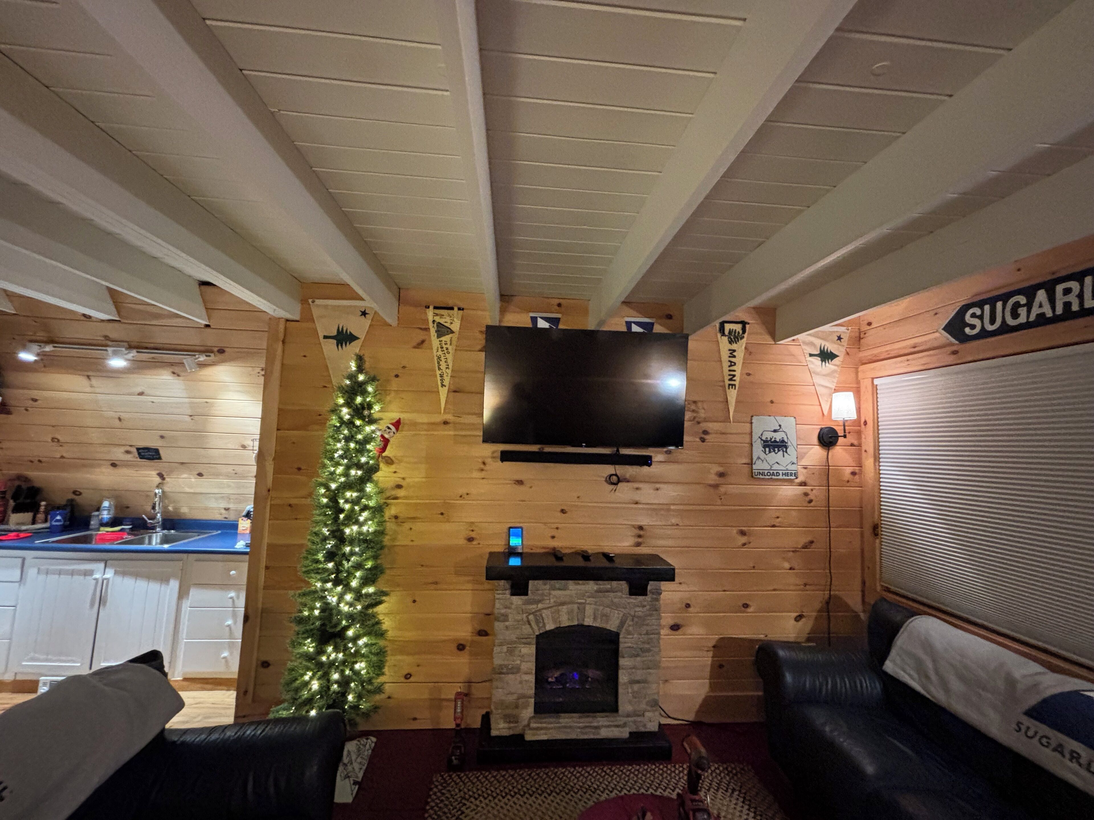 A cozy living room with a fireplace, a Christmas tree, and a television mounted on the wall.
