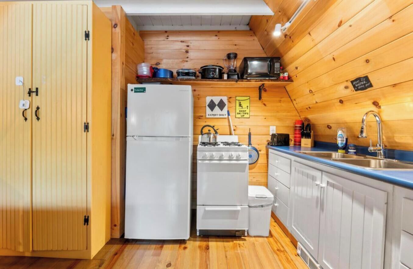A compact kitchen with wooden walls, a white refrigerator, a stove, and a sink.