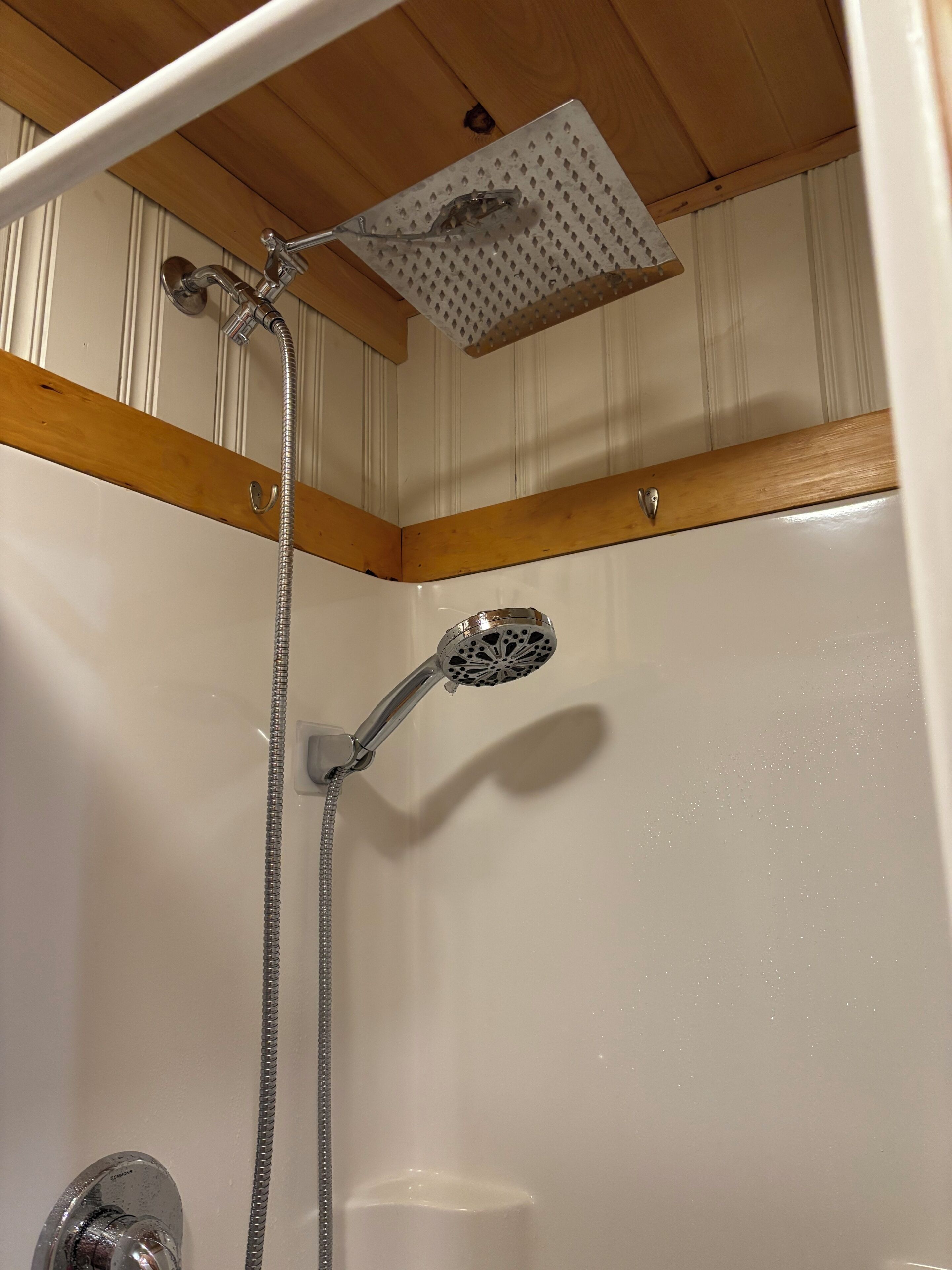 A shower with a handheld showerhead and a fixed showerhead, both mounted on a wall with a wooden beam above.