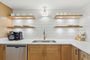 A kitchen with a stainless steel sink, wooden cabinets, a coffee maker, and glassware on shelves. - 1st floor gulf-front condo in Ft Walton Bch FL (Fort Walton Beach)