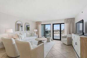 A modern living room with a sofa, chairs, a coffee table, a TV, and a balcony with a view. - 1st floor gulf-front condo in Ft Walton Bch FL (Fort Walton Beach)