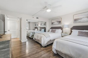 Quarto de hotel com duas camas, um ventilador de teto, um espelho grande e obras de arte nas paredes.