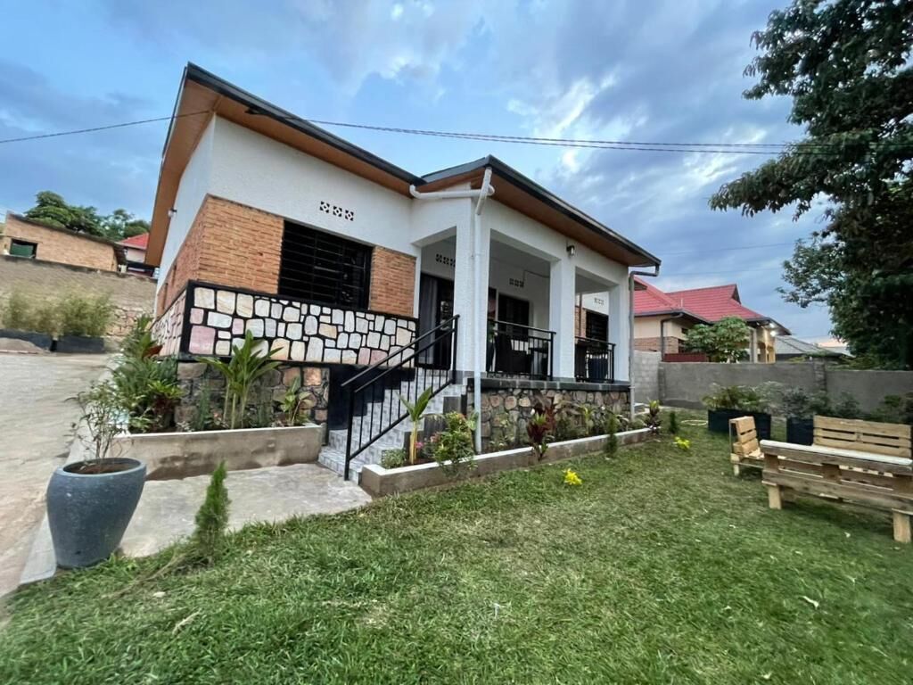 A two-story house with a covered porch, a stone facade, and a small garden area with a bench.