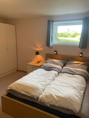 A bedroom with a bed, nightstands, a lamp, a window with curtains, and a wardrobe. - Leilighet i solfylte Mandal (Agder)