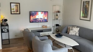 A modern living room with a grey sofa, a white coffee table, and a flat-screen TV displaying a fire scene.