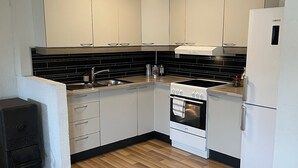 A compact kitchen with white cabinets, a black tiled backsplash, a built-in oven, and a white refrigerator.