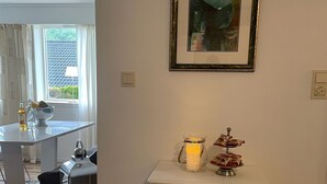 A white bedside table with a drawer, a small lamp, and a framed picture on the wall.