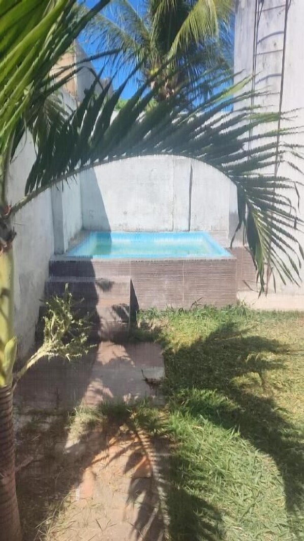 A swimming pool with a concrete wall and steps leading up to it, surrounded by grass and palm trees. - Pousada Refúgio Praia & Café (Beberibe)