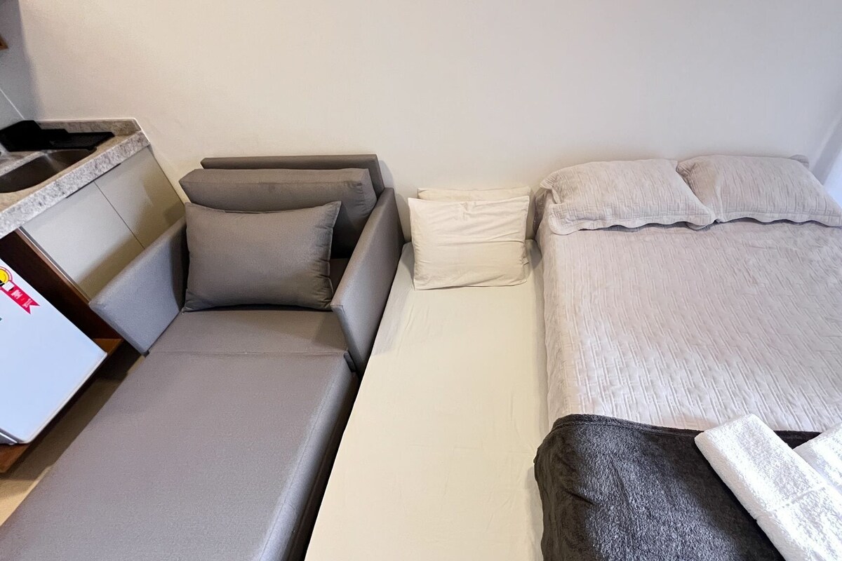 A single room with a bed, a small table, and a window with blinds.