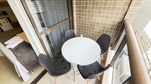 A small balcony with a round table and four chairs, a towel on the floor, and a view of the cityscape. - Terrazza Beach Residence - Praia dos Carneiros (Tamandaré)
