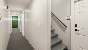 Un couloir moderne avec un mur vert au fond, une porte blanche dotée d’une serrure numérique et un escalier muni d’une main courante.
