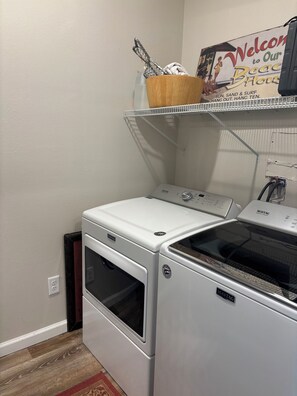 A laundry room with a Maytag washer and dryer, a wooden shelf with a basket, and a welcome sign. -  2 Min Walk to the Beach - Sleeps 6 - 3BR Townhome with Private Outdoor Shower (Mexico Beach)