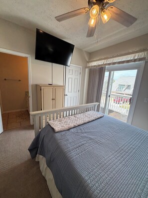 Un dormitorio con cama, ventilador de techo, televisor y vistas al exterior.