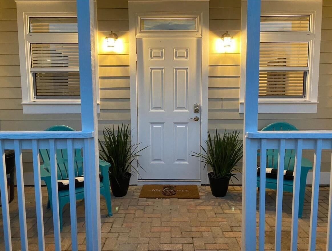 A front door with a welcome mat, potted plants, and a porch railing.