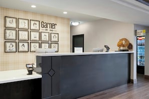 Ein Hotel-Rezeptionsbereich mit Theke, gerahmten Kunstwerken an der Wand, einem Kühlschrank und einer Kasse.