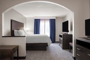 Ein Hotelzimmer mit Bett, Schreibtisch, Fernseher und einem Vorhangfenster.