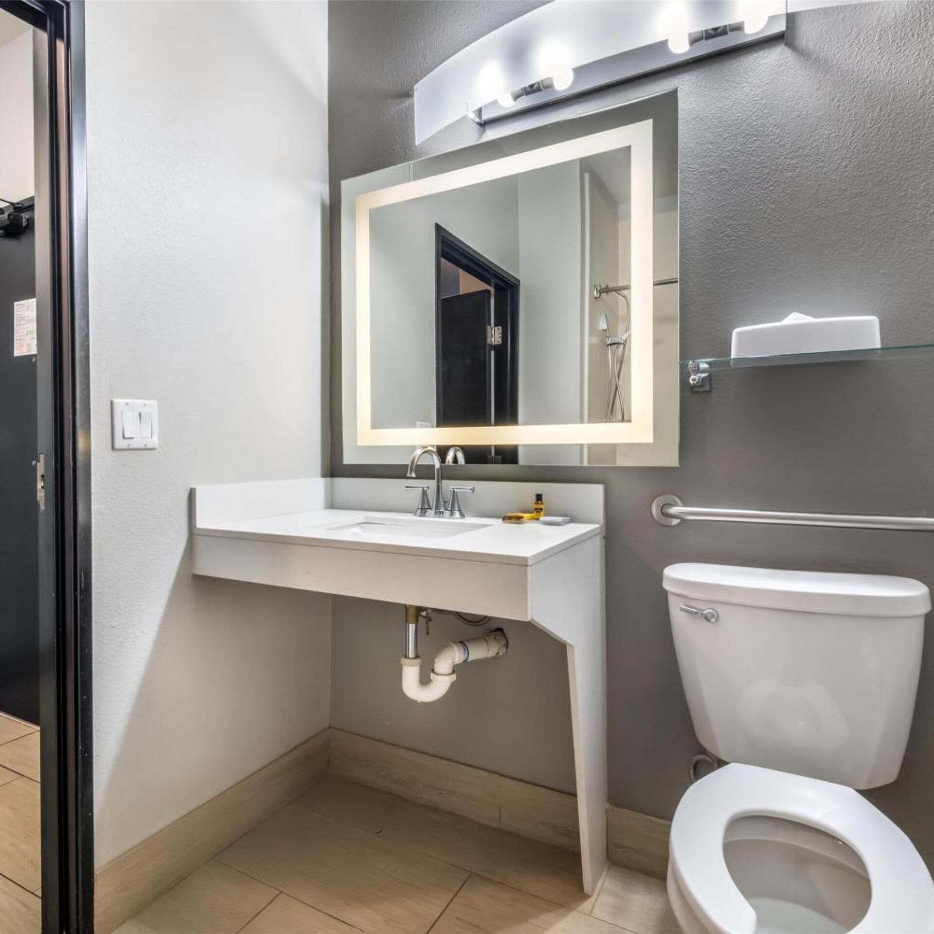 A bathroom with a white sink, a mirror with lights, a toilet, and a shower area.