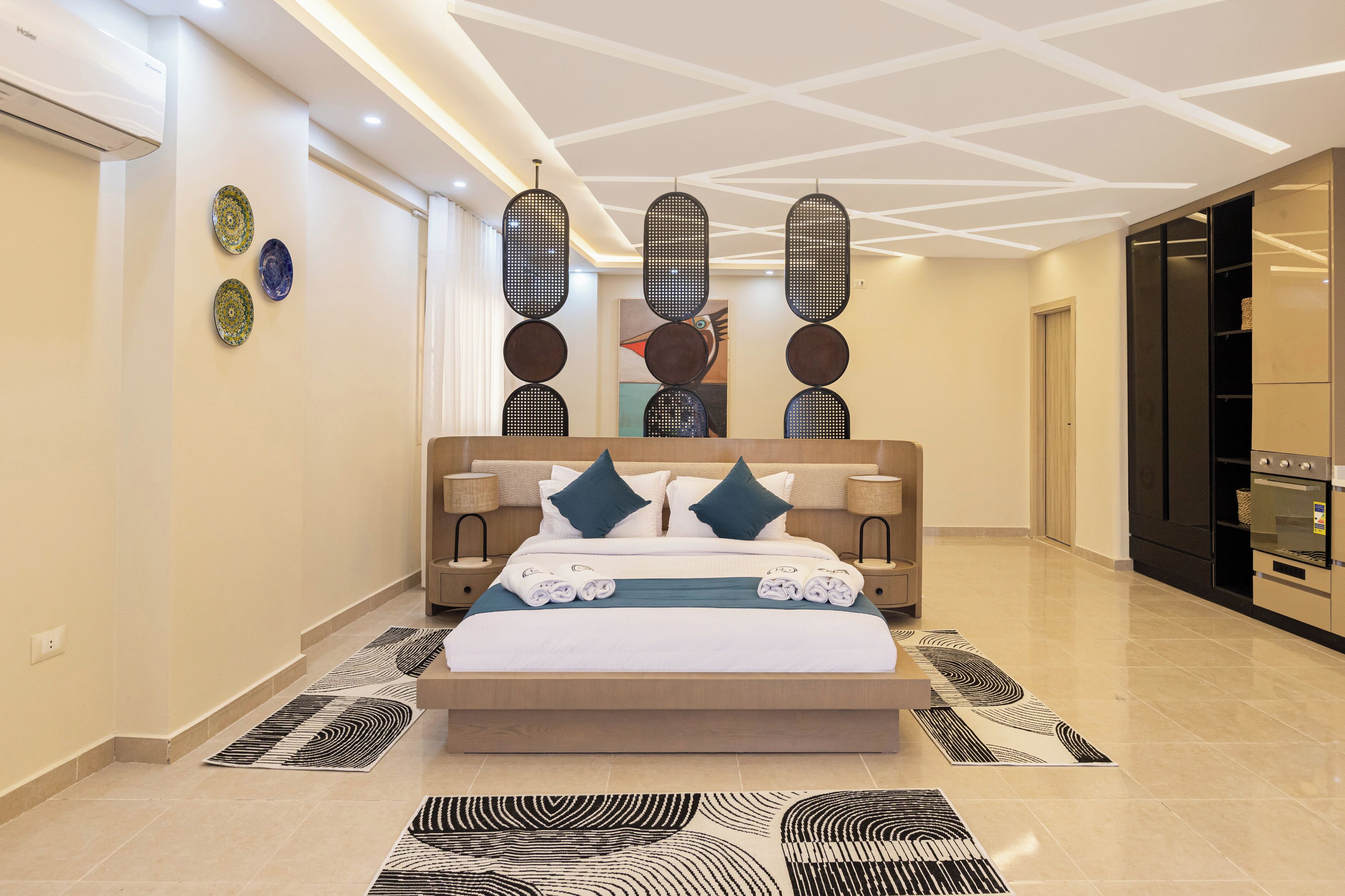 A modern bedroom with a large bed, bedside tables, a built-in wardrobe, and a kitchen area.