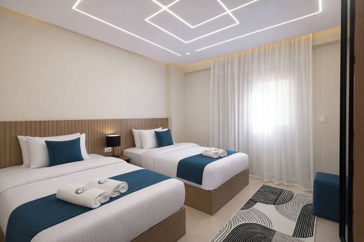 Ein Hotelzimmer mit zwei Betten, einem modernen Deckenstil und einem großen Fenster mit Vorhängen.