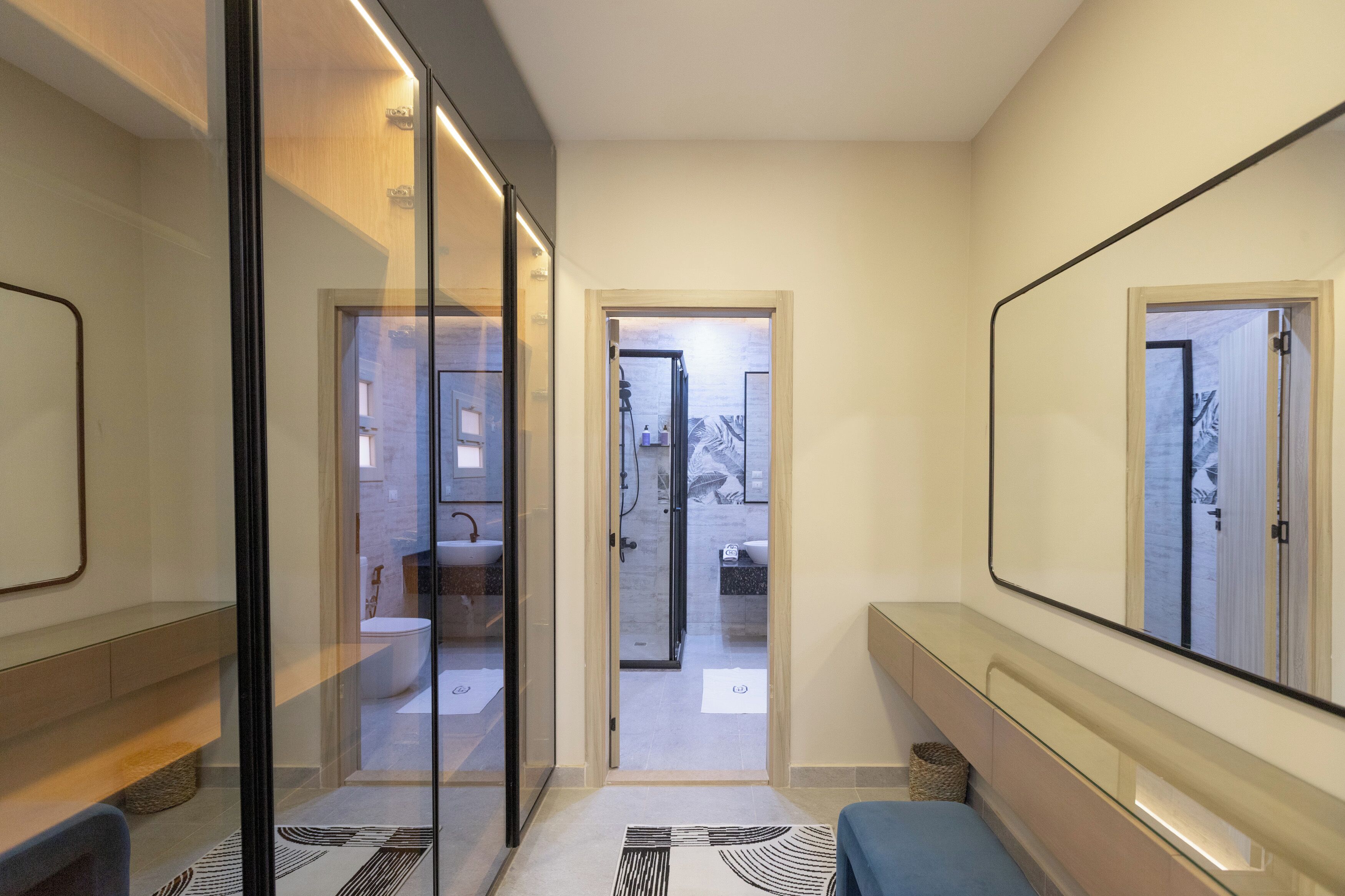 A modern bathroom with a glass partition, a bench, and a large mirror.