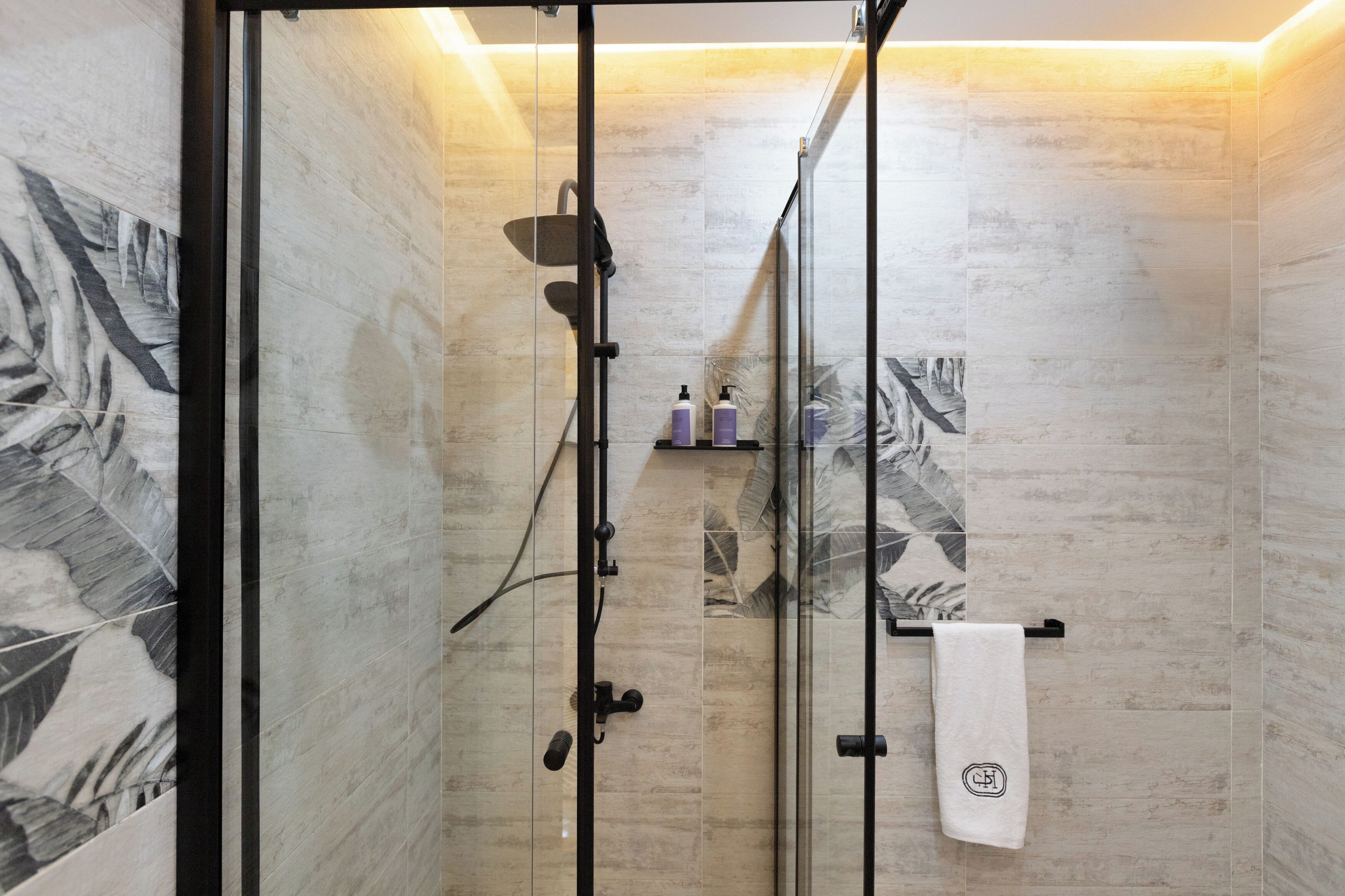 A glass-enclosed shower with a towel rack and toiletries.