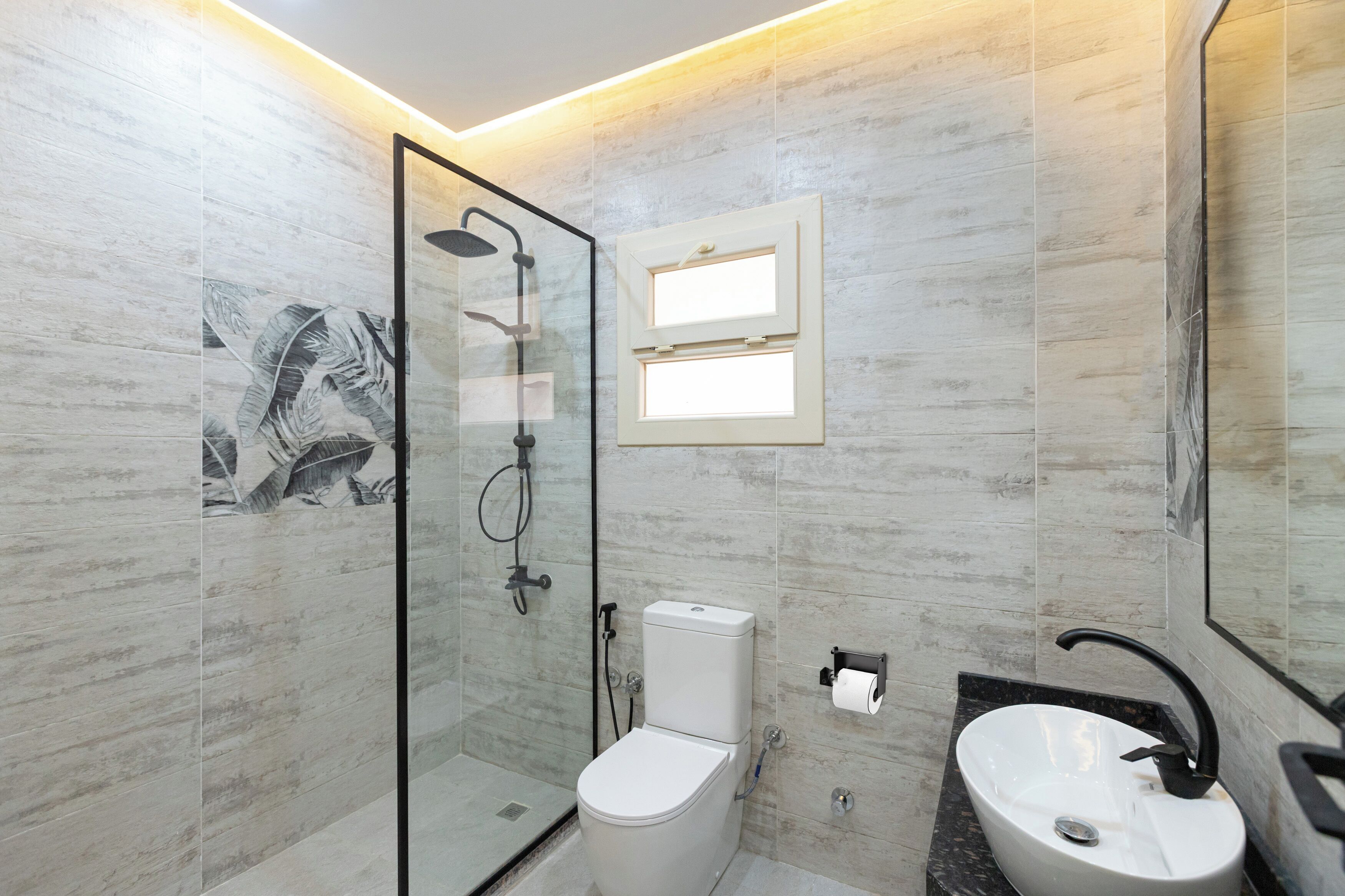 Un baño moderno con cabina de ducha de vidrio, inodoro y lavamanos con grifo negro.