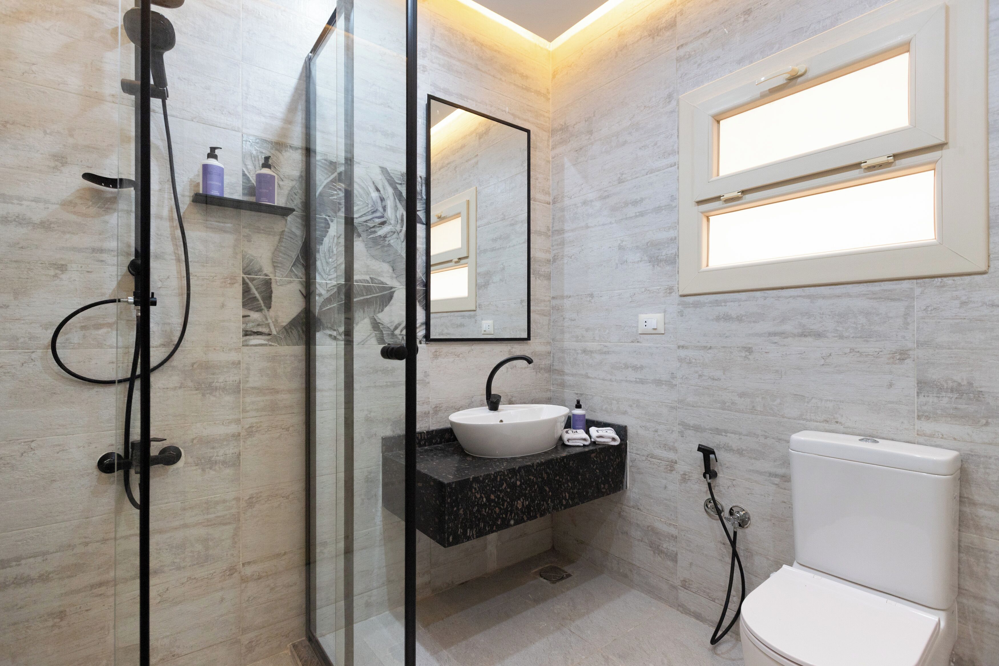 Un baño moderno con cabina de ducha de vidrio, un lavabo blanco y un inodoro.