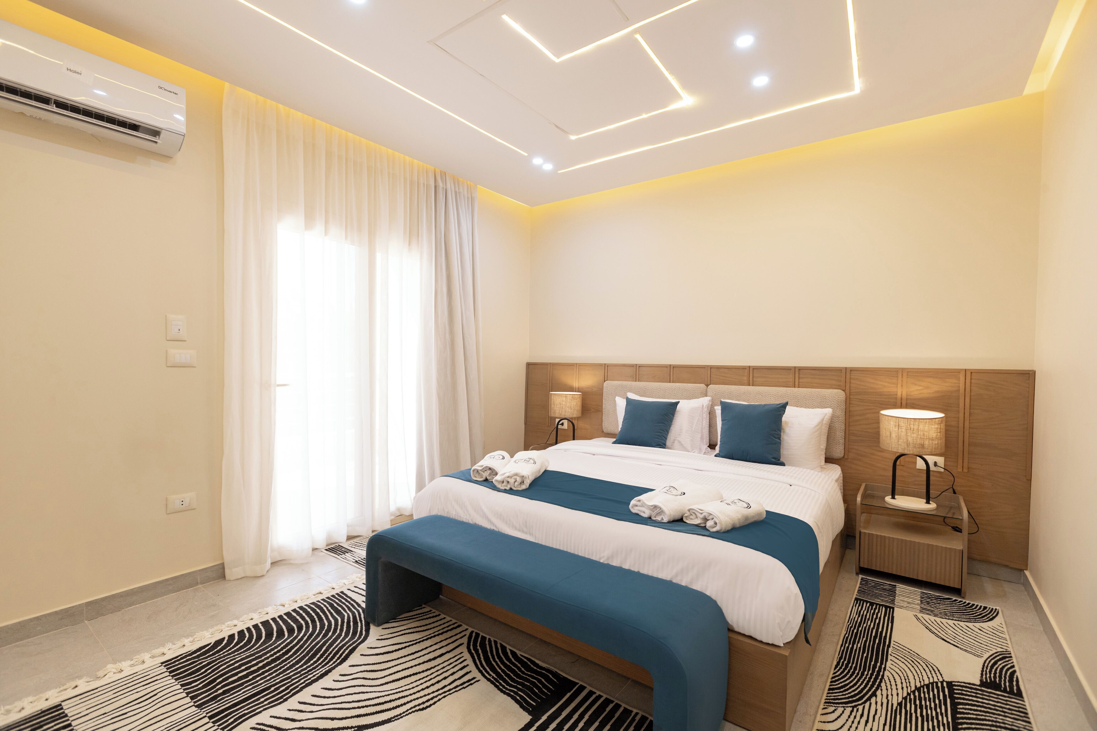 A modern hotel room with a neatly made bed, a bedside table with a lamp, and a large window with curtains.