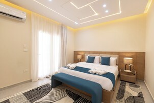 A modern hotel room with a neatly made bed, a bedside table with a lamp, and a large window with curtains.