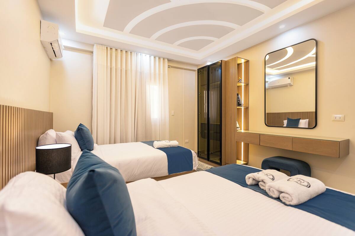 Ein Hotelzimmer mit zwei Betten, einem großen Spiegel, einem Nachttisch mit Lampe und einem Kleiderschrank.