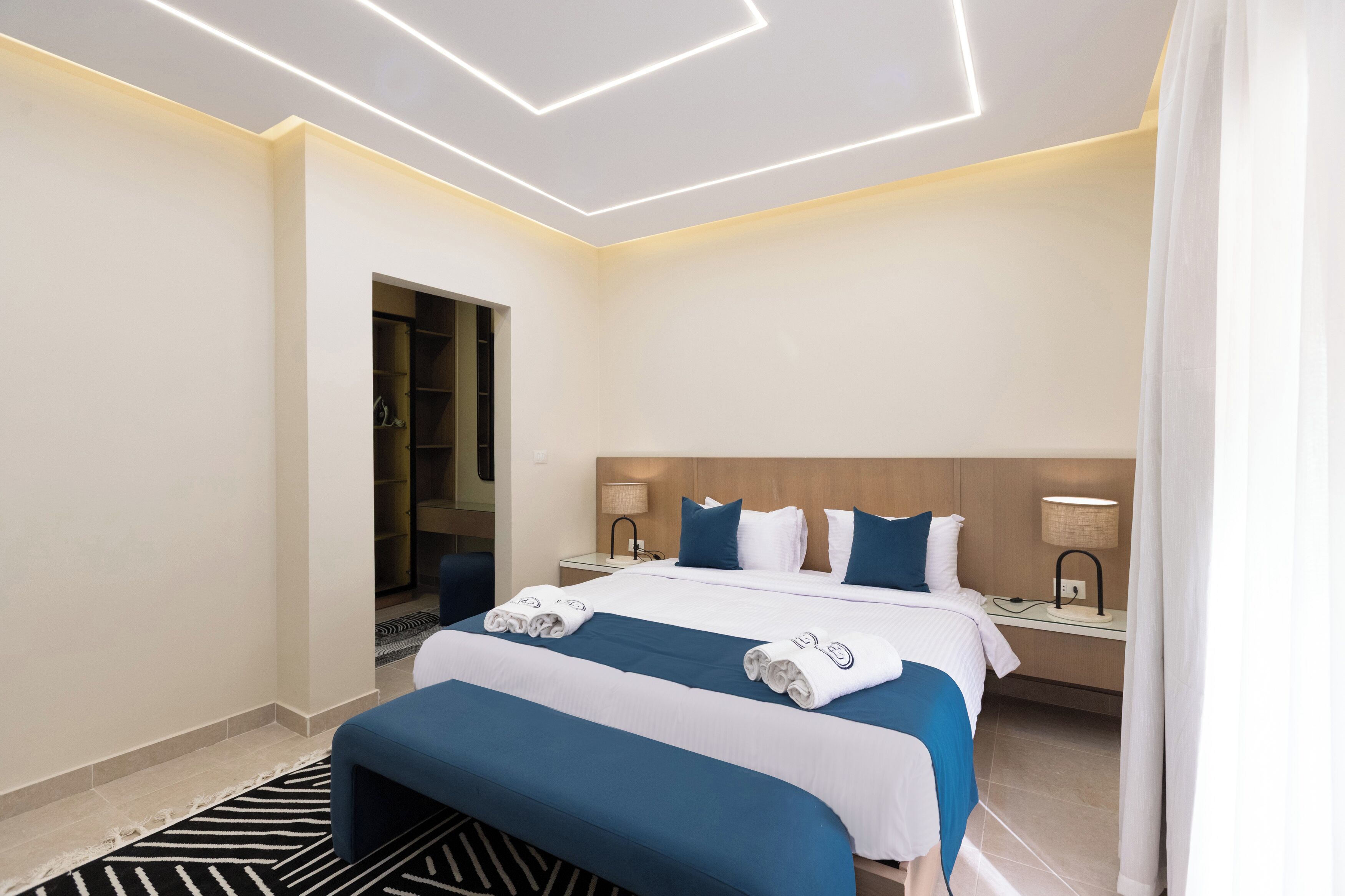 Ein Hotelzimmer mit einem ordentlich bezogenen Bett, einem Nachttisch mit Lampe und einer Tür zu einem Badezimmer.
