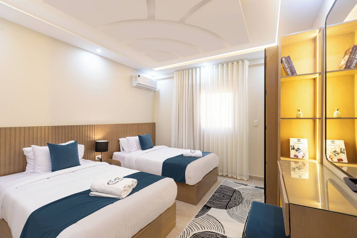 Ein Hotelzimmer mit zwei Betten, einem Schreibtisch, einem Spiegel und einem Bücherregal mit Büchern und Dekoration.