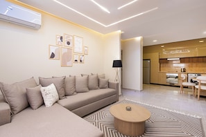 A modern living room with a sectional sofa, a coffee table, and a kitchen area in the background. - Beithady Luxury Aparthotel Lotus - BH-73 (New Cairo)