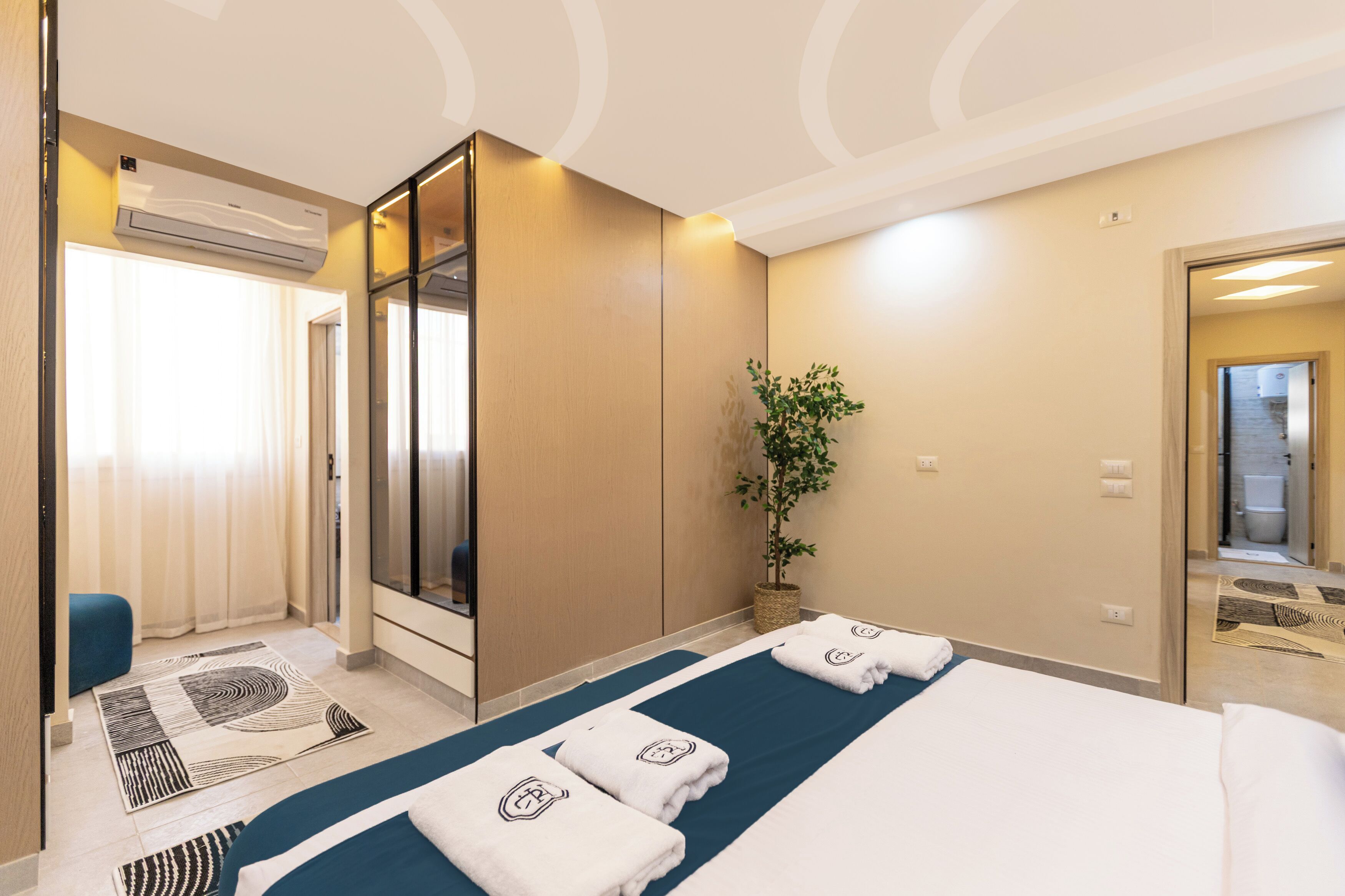 Habitación de hotel con cama, escritorio, aire acondicionado, espejo y planta en maceta.