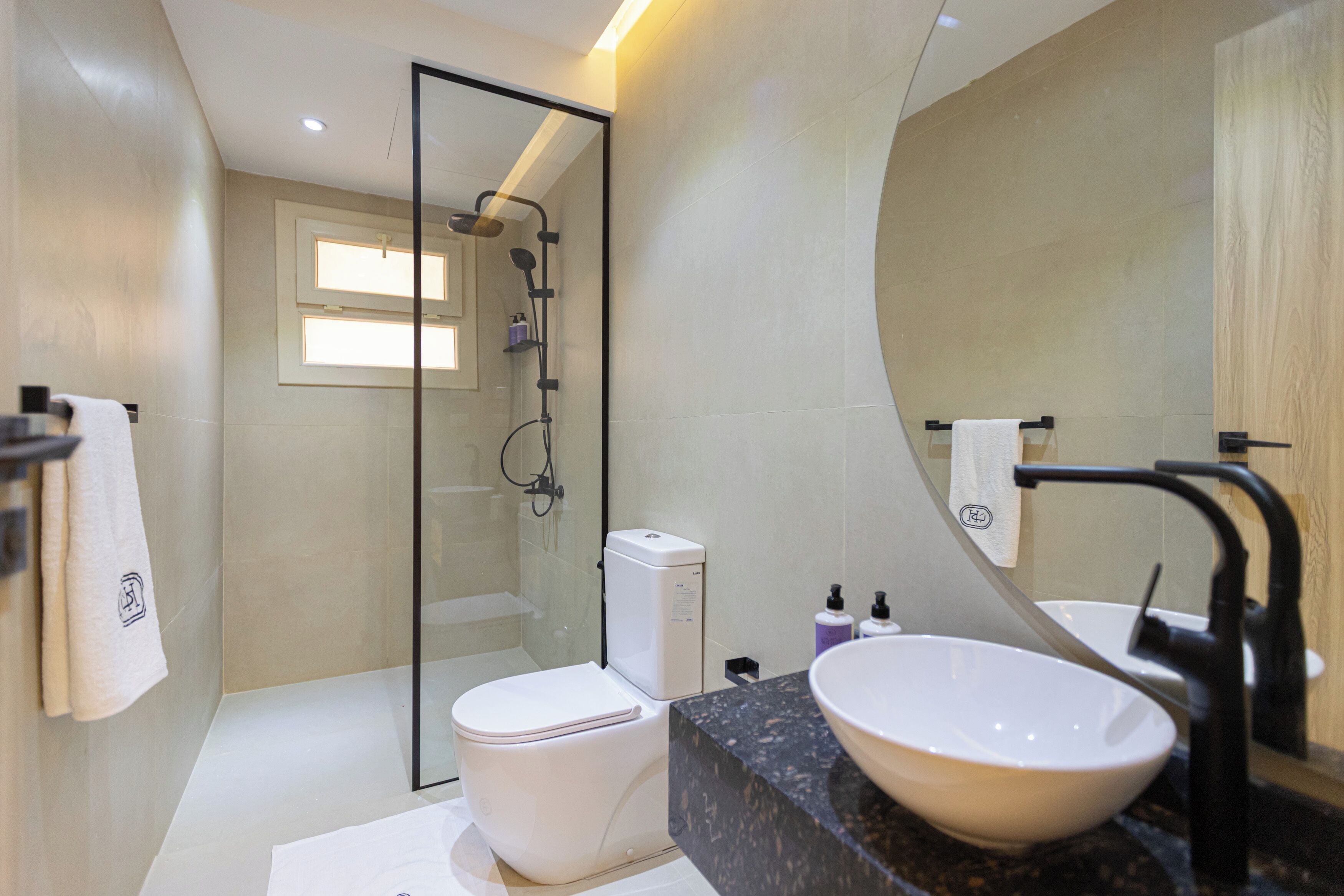 Un baño moderno con ducha de vidrio, inodoro blanco y lavamanos grande con grifo negro.