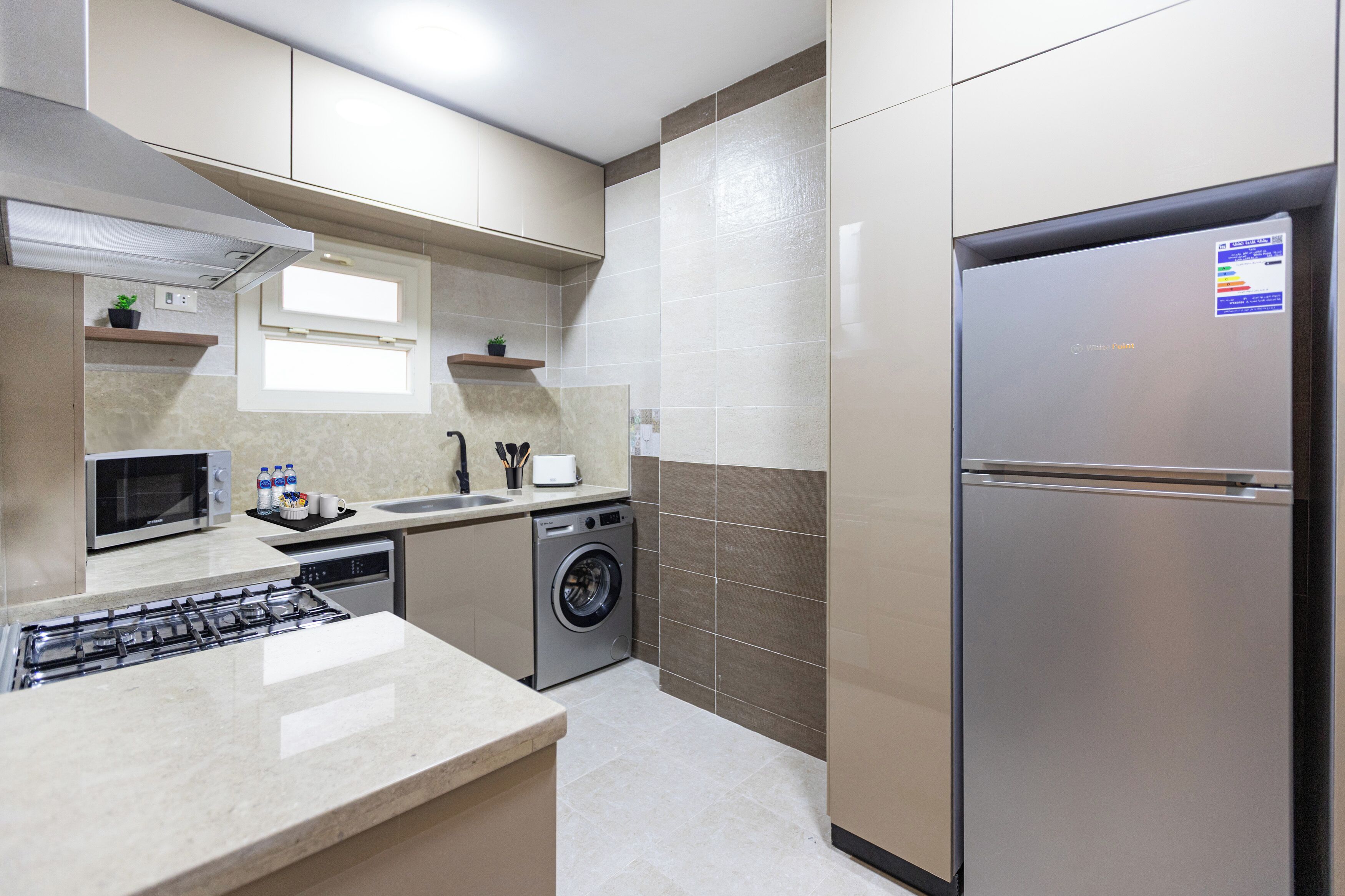 Eine moderne Küche mit einem Edelstahl-Kühlschrank, einem eingebauten Backofen, einer Mikrowelle, einer Waschmaschine und einem Gasherd.
