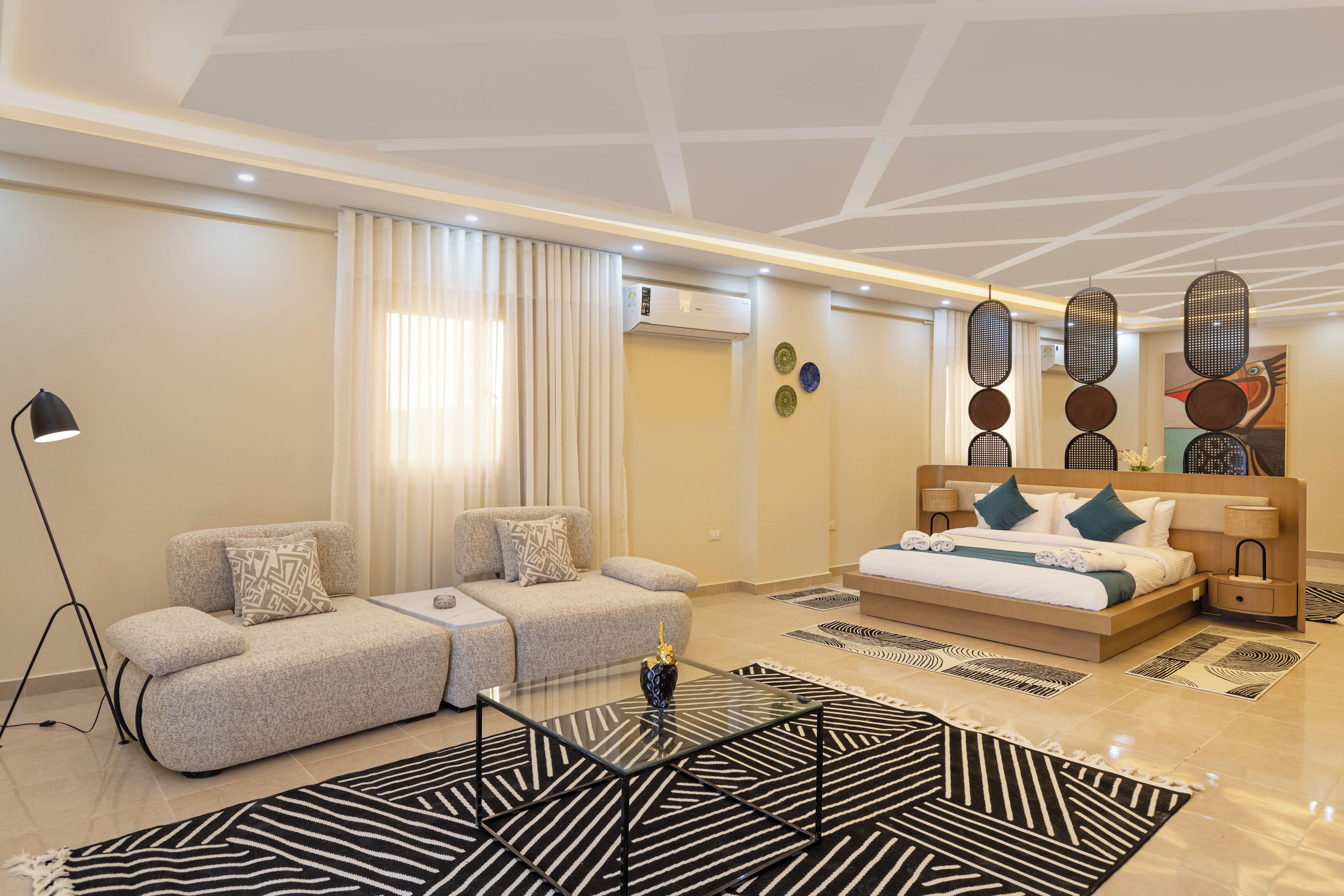 Una habitación de hotel moderna con sofá, cama, una mesa de centro de vidrio y una alfombra estampada.