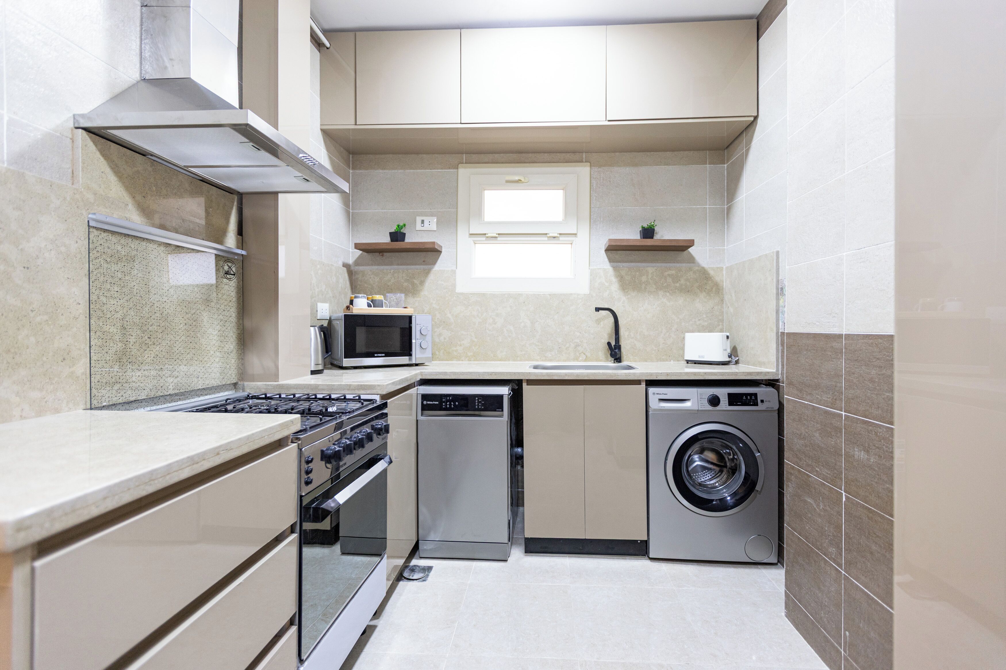 Een compacte keuken met een gasfornuis, magnetron, vaatwasser en wasmachine.