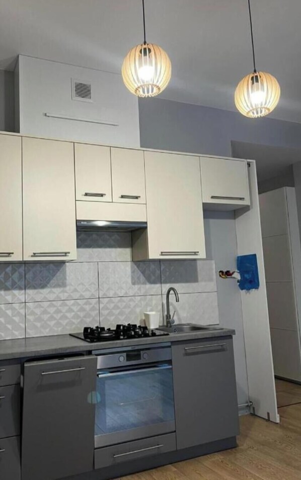 A modern kitchen with white cabinets, a gas stove, an oven, and two pendant lights.