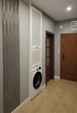 A laundry room with a washing machine and dryer, a door, and patterned wallpaper.