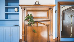 A room with a wooden fireplace, a clock on the mantel, and a blue wall with shelves. - Stylish Historic Acton Apartment (London)