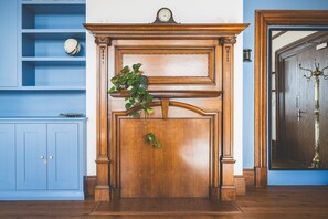 Ein Zimmer mit Kamin aus Holz, einer Uhr auf dem Kaminvorsatz und einer blauen Wand mit Regalen.